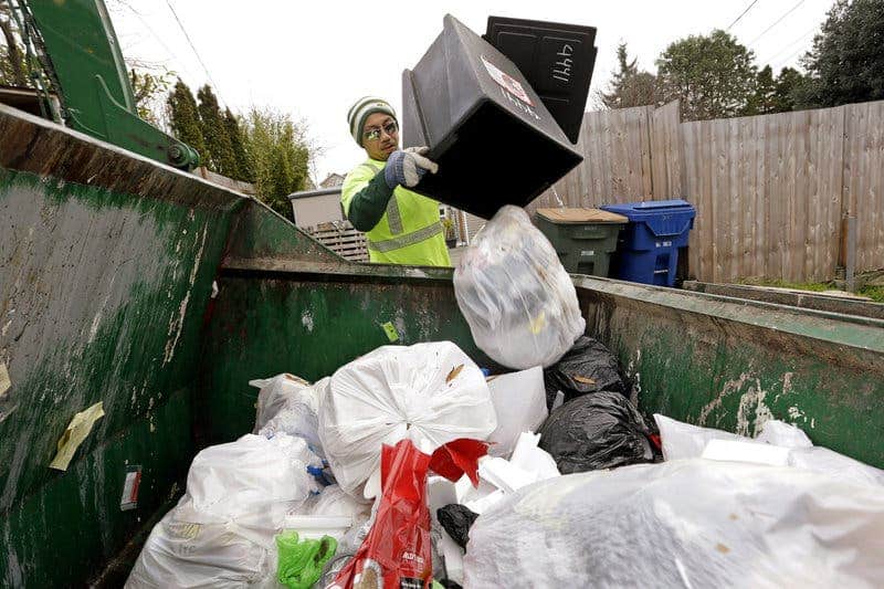 Seattle garbage collector Anousone Sadettanh empties a small residential garbage bin into his truck in 2014. It is now illegal to toss out food with the trash in the city. Residents will get warning tags for now; the city will start imposing fines in July. Elaine Thompson/AP