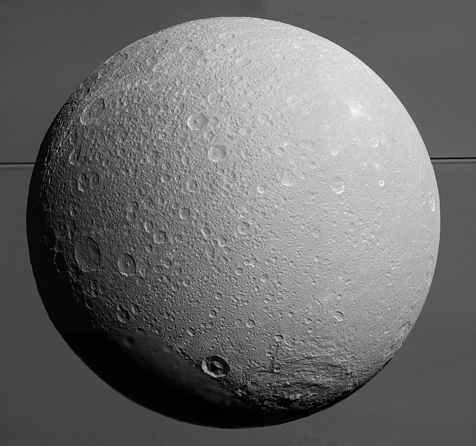 This view from NASA’s Cassini spacecraft looks toward Saturn’s icy moon Dione, with giant Saturn and its rings in the background, just prior to the mission’s final close approach to the moon on 17 August 2015. At lower right is the large, multi-ringed impact basin named Evander, which is about 220 miles (350 kilometres) wide. The canyons of Padua Chasma, features that form part of Dione’s bright, wispy terrain, reach into the darkness at left. Image credit: NASA/JPL-Caltech/Space Science Institute.