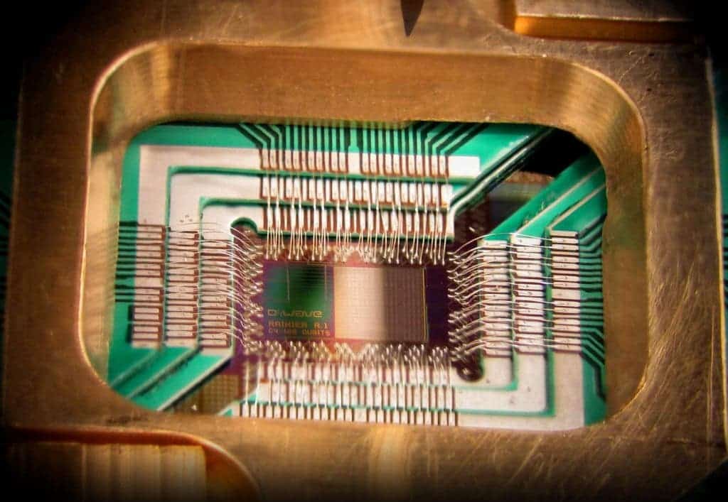 Photograph of a chip constructed by D-Wave Systems Inc., mounted and wire-bonded in a sample holder. The D-Wave processor is designed to use 128 superconducting logic elements that exhibit controllable and tunable coupling to perform operations. Image via Wikipedia.