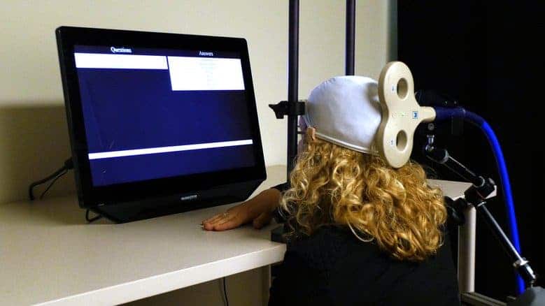 University of Washington postdoctoral student Caitlin Hudac wears a cap that uses transcranial magnetic stimulation (TMG) to deliver brain signals from the other guessing-game participant. (University of Washington)