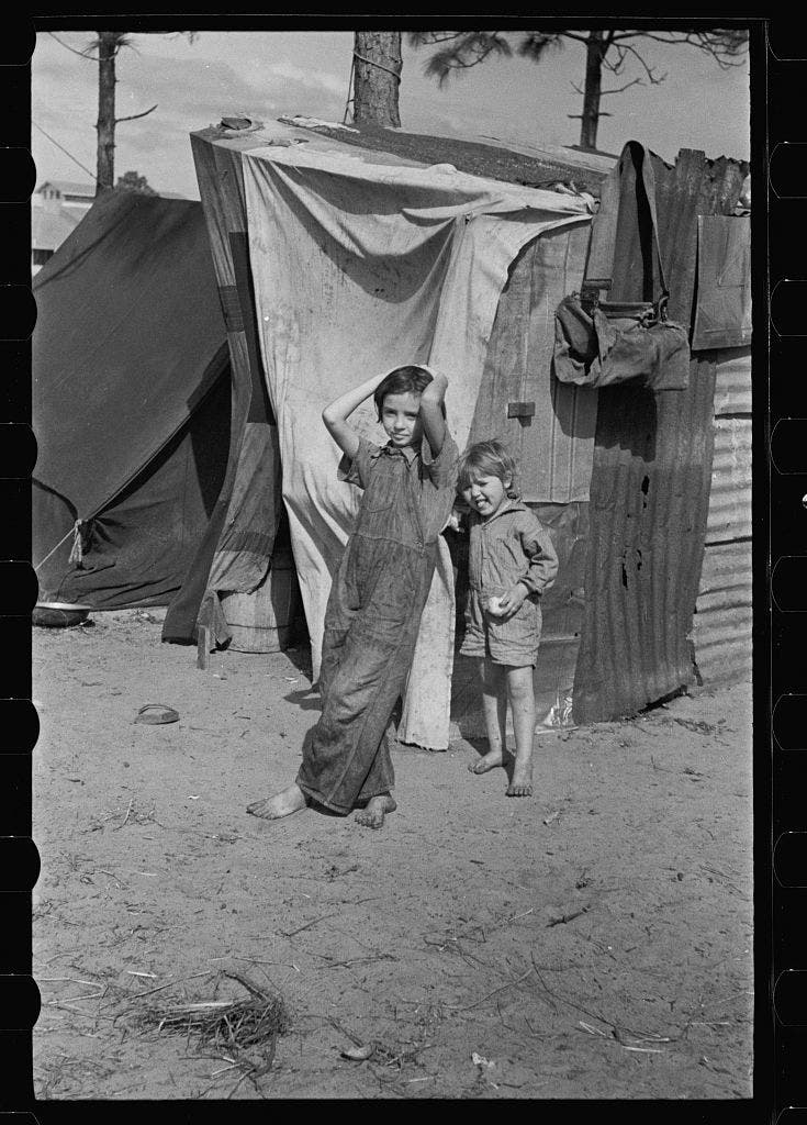 Two children of a migrant fruit worker from Tennessee, standing before their temporary home. This family of eight is camped in a field near the packinghouse at Winter Haven, Florida