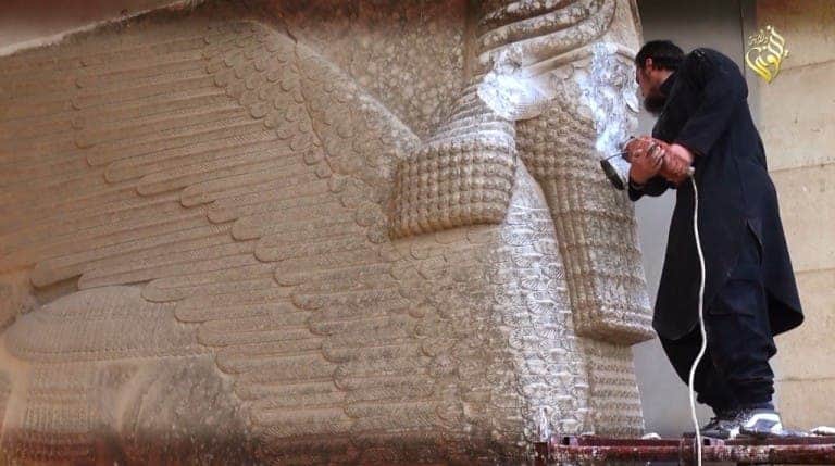 A member of ISIS destroying an ancient Assyrian lamassu (screenshot from an ISIS propaganda video).
Image via hyperallergic