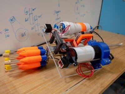 View showing eight orange spear tips mounted on the blue carousel, two small boxes just behind the carousel containing cameras, the electronics chamber behind the right camera, and the buoyancy chamber behind the left camera. Credit: WPI.
