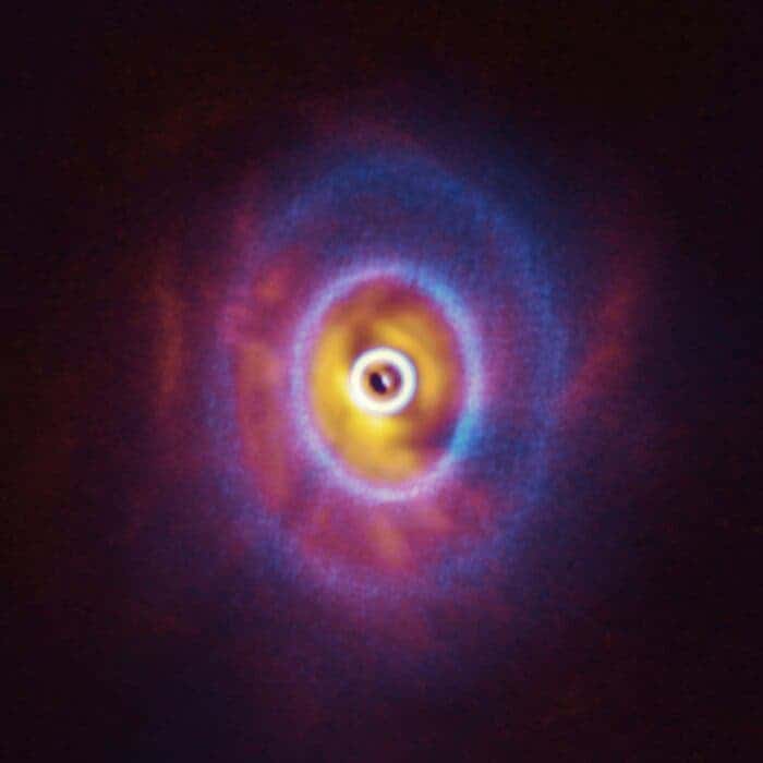 ALMA, in which ESO is a partner, and the SPHERE instrument on ESO’s Very Large Telescope have imaged GW Orionis, a triple star system with a peculiar inner region. Unlike the flat planet-forming discs we see around many stars, GW Orionis features a warped disc, deformed by the movements of the three stars at its centre. This composite image shows both the ALMA and SPHERE observations of the disc. The ALMA image shows the disc’s ringed structure, with the innermost ring (part of which is visible as an oblong dot at the very centre of the image) separated from the rest of the disc. The SPHERE observations allowed astronomers to see for the first time the shadow of this innermost ring on the rest of the disc, which made it possible for them to reconstruct its warped shape. (ESO/Exeter/Kraus et al., ALMA (ESO/NAOJ/NRAO))
