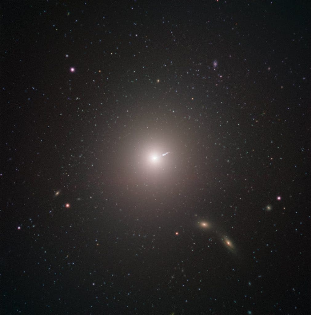 Messier 87 (M87) is an enormous elliptical galaxy located about 55 million light years from Earth, visible in the constellation Virgo. It was discovered by Charles Messier in 1781, but not identified as a galaxy until 20th Century. At double the mass of our own galaxy, the Milky Way, and containing as many as ten times more stars, it is amongst the largest galaxies in the local universe. Besides its raw size, M87 has some very unique characteristics. For example, it contains an unusually high number of globular clusters: while our Milky Way contains under 200, M87 has about 12,000, which some scientists theorise it collected from its smaller neighbours. Just as with all other large galaxies, M87 has a supermassive black hole at its centre. The mass of the black hole at the centre of a galaxy is related to the mass of the galaxy overall, so it shouldn’t be surprising that M87’s black hole is one of the most massive known. The black hole also may explain one of the galaxy’s most energetic features: a relativistic jet of matter being ejected at nearly the speed of light. The black hole was the object of paradigm-shifting observations by the Event Horizon Telescope. The EHT chose the object as the target of its observations for two reasons. While the EHT’s resolution is incredible, even it has its limits. As more massive black holes are also larger in diameter, M87's central black hole presented an unusually large target—meaning that it could be imaged more easily than smaller black holes closer by. The other reason for choosing it, however, was decidedly more Earthly. M87 appears fairly close to the celestial equator when viewed from our planet, making it visible in most of the Northern and Southern Hemispheres. This maximised the number of telescopes in the EHT that could observe it, increasing the resolution of the final image. This image was captured by FORS2 on ESO’s Very Large Telescope as part of the Cosmic Gems programme, an outreach initiative that (ESO)
