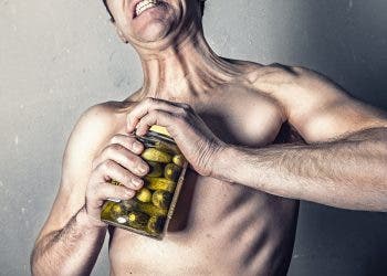 Stock photo of a man trying to exaggeratedly open a jar of pickles.