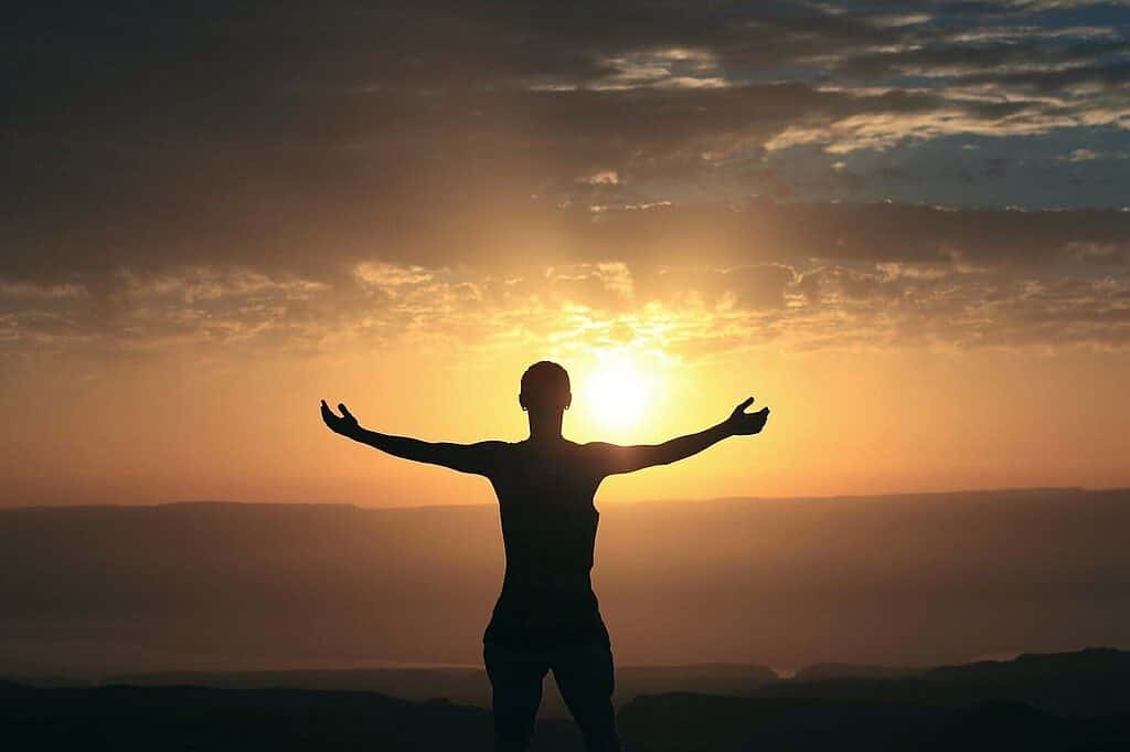 Silhouette of a woman during dawn with her hands stretched out on each side as if she is hugging the sun.