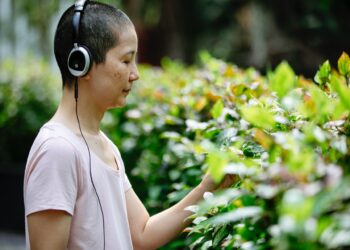 A woman touching plants while listening to music on headphones.