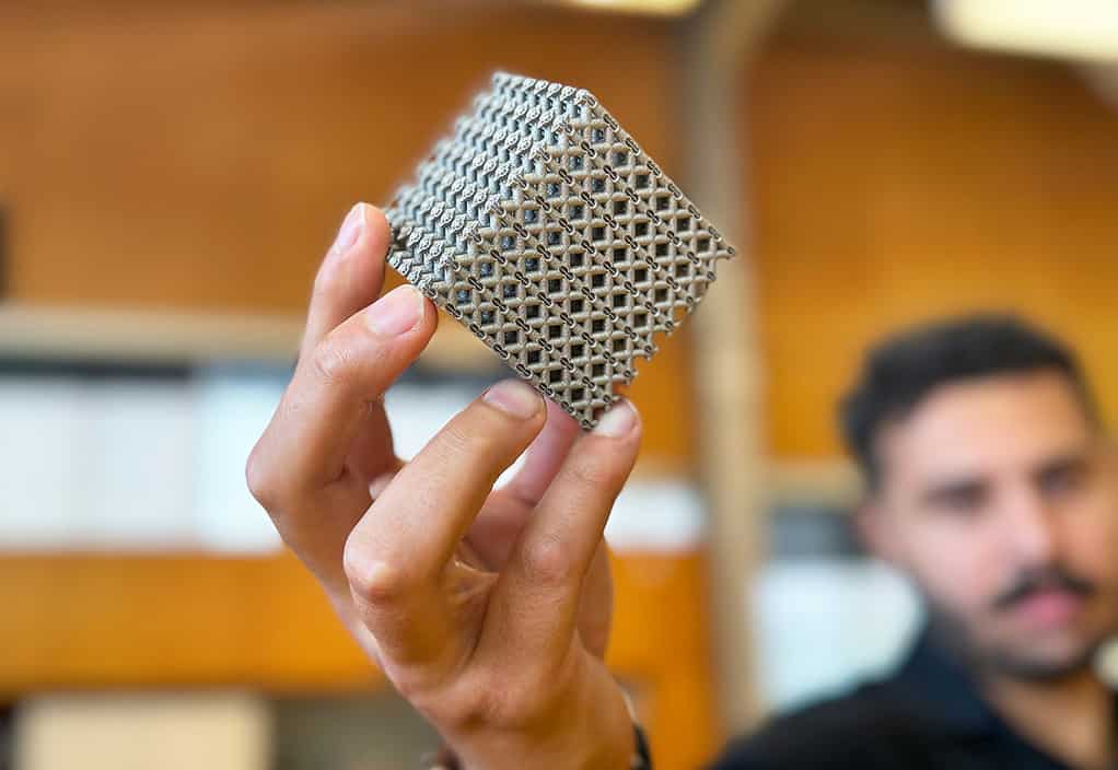 Ph.D. candidate Jordan Noronha holding a titanium lattice structure sample 3D printed in cube form.