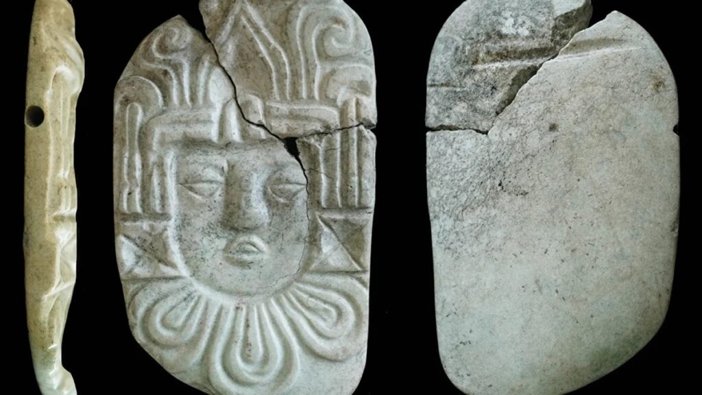 Los objetos quemados encontrados en una pirámide maya con huesos reales cremados incluían una placa colgante con una cabeza humana tallada.  C. Halperin/Cortesía de Antigüedad